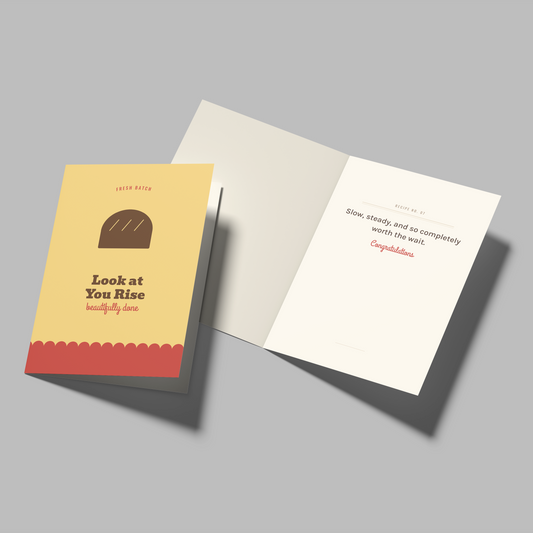 A set of greeting cards displayed on a neutral gray background. One card is shown closed from the front, featuring a warm yellow background, a brown loaf of bread illustration, and the text 'Look at You Rise' with 'kindly yours' at the bottom.