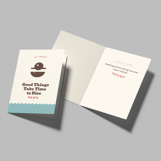 A folded greeting card and its matching envelope on a neutral gray background. The card cover is white with a dark brown illustration of a coffee cup and the text 'Good Things Take Time to Rise' in dark brown and red.