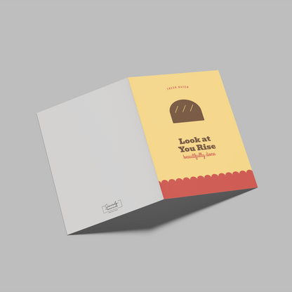 An open greeting card or booklet shown on a plain gray background. The right panel is pale yellow with a brown loaf illustration, the text 'Look at You Rise' and smaller decorative text, and a coral-red scalloped band at the bottom.