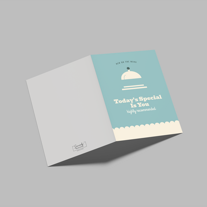 A folded square paper card or booklet shown open on a plain gray background. The right panel is light aqua with a white teapot illustration and the text 'Put the Kettle On just for you'; the left panel is white with a small logo near the bottom.