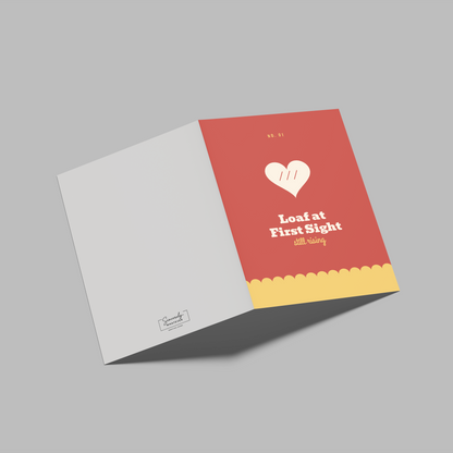 A folded greeting card shown open on a plain gray background. The right panel is coral red with a white heart logo, the text 'Love at First Sight' and 'Will Smith,' plus a yellow scalloped band at the bottom.