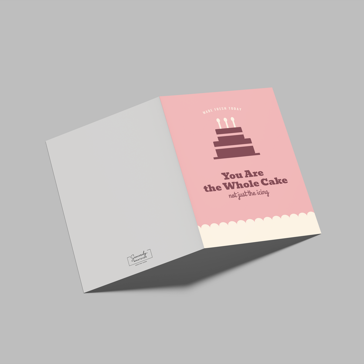 An open greeting card or invitation shown on a plain gray background. The left panel is light gray, and the right panel is pink with a dark cake illustration and the text 'You Are the Whole Cake' and 'cut out for me.