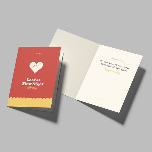 An open greeting card and its matching red cover shown on a plain gray background. The cover reads 'Loaf at First Sight' with a white heart and small yellow text.