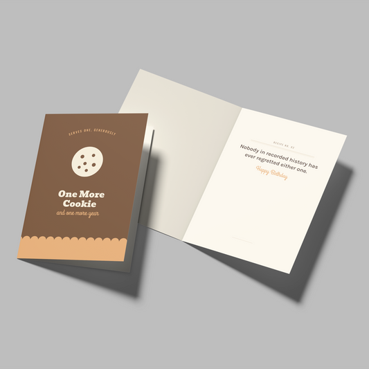 A greeting card set shown on a neutral gray background, featuring a brown envelope-style card labeled 'One More Cookie' and an open white card with printed text on the inside.