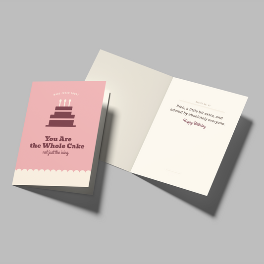 A birthday greeting card set shown on a neutral gray background. The set includes a pink card with a tiered cake illustration and the text 'You Are the Whole Cake and just the cake' next to an open white card with a message for the recipient.